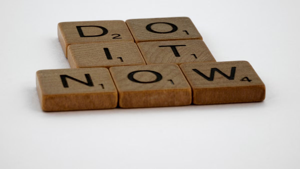 Wooden Scrabble tiles spelling 'Do It Now' on a white background. Motivational concept.